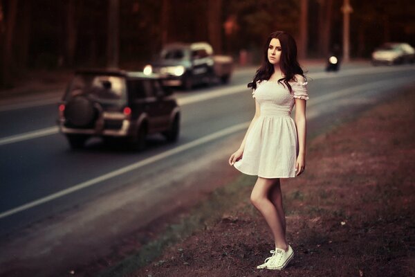 A girl in a white dress on the side of the road near the highway