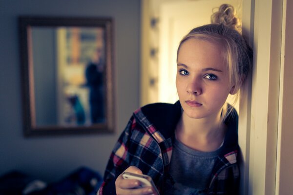 A teenage girl with a thoughtful look and an iPhone in her hands