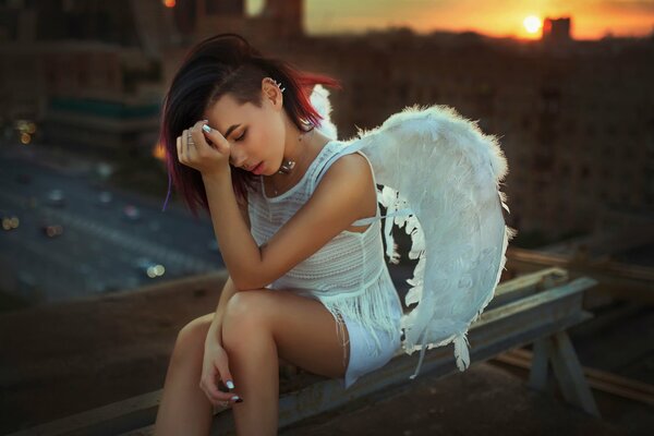 A girl in the role of an angel sits on the background of the road