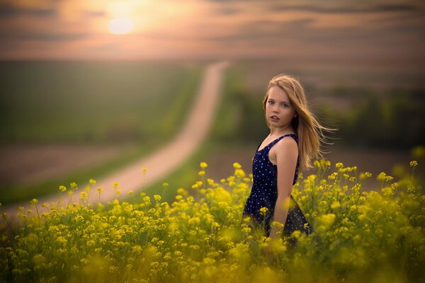 A girl in a field by the road at sunset