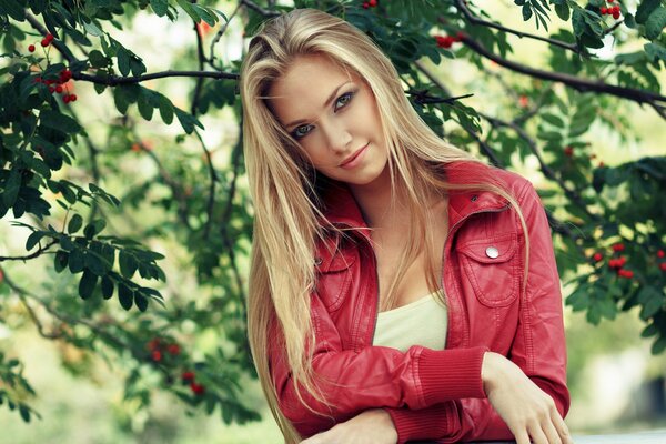 Belle fille blonde en veste rouge avec un regard envoûtant sur fond de branches d arbre avec feuillage vert et baies rouges