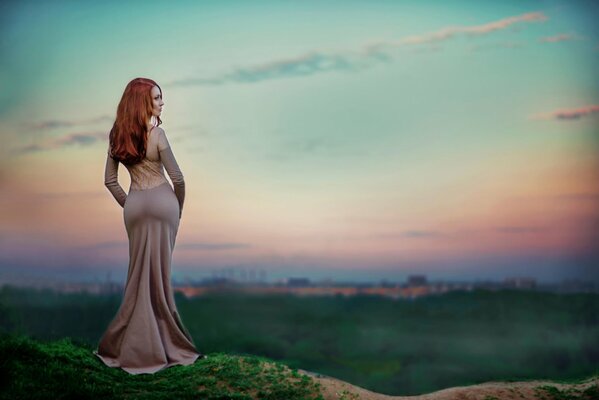 Femme mince Rousse en robe de soirée sur fond de coucher de soleil