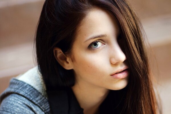 Beau modèle aux yeux bleus aux cheveux noirs Emily Rudd couvrant l œil gauche avec une mèche de cheveux mignon regarde dans le cadre