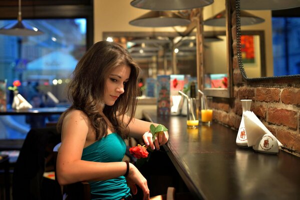 Mädchen sitzt in einer bar mit einer Rose in der Hand