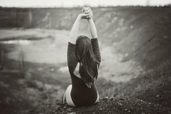 Black and white photo of a girl from the back sitting on the edge of a cliff