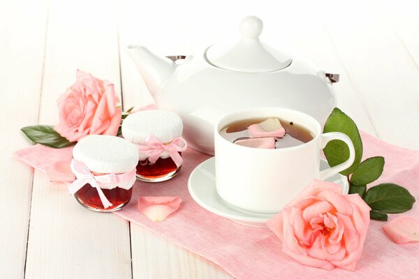 A white teapot with a cup and dishes, next to jam