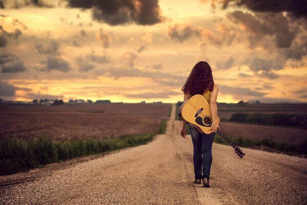 A girl walking freely on the road with a guitar