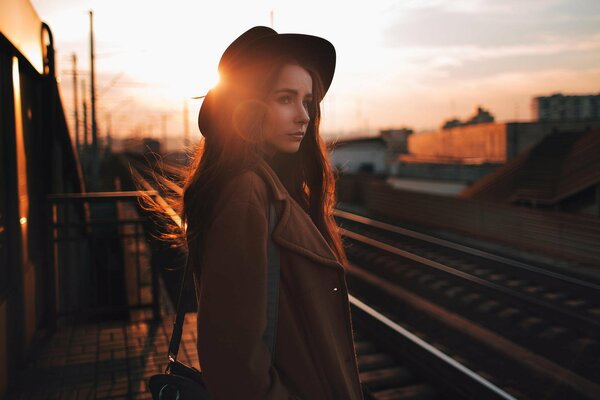 Portrait d une jeune fille au chapeau sur le chemin de fer pendant le coucher du soleil