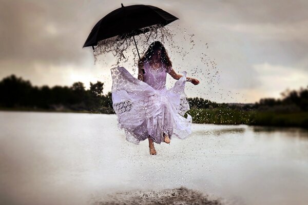 A girl under an umbrella jumps through puddles