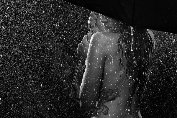 Naked girl from behind in the rain under a black umbrella with her hair down and a tattoo on her left side black and white photo