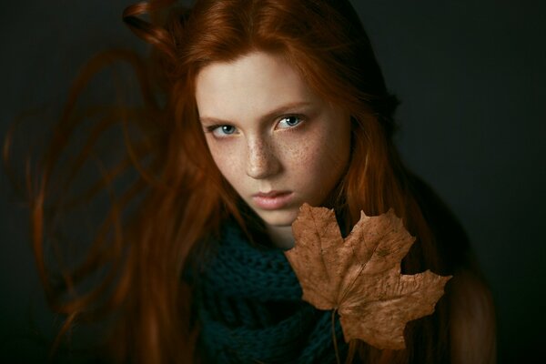 Fille Rousse avec des taches de rousseur dans une écharpe verte tricotée tenant une feuille d érable orange sèche