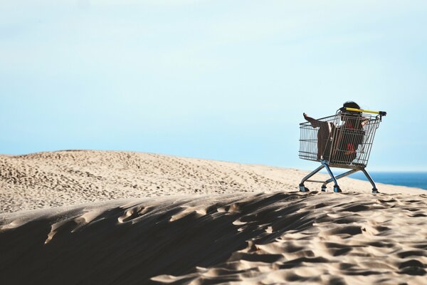 A girl is sitting in a shopping cart from a shopping center on the seashore