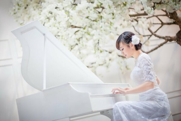 Asiatische Mädchen im weißen Kleid spielt auf einem weißen Klavier auf weißem Hintergrund