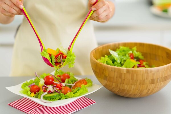 Hände legen grünen Salat auf einen Teller