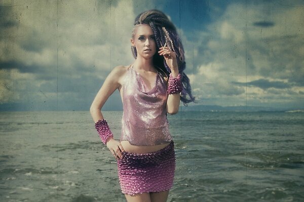 A girl with dreadlocks and a cigarette in her hands against the background of the sea