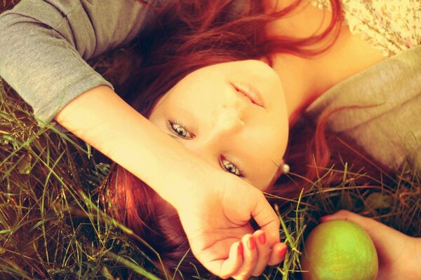 Foto tematica. Ragazza con i capelli rossi nelle mele. Dolce ragazza si trova sull erba