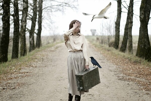 A girl with a suitcase in her hands is walking along the road