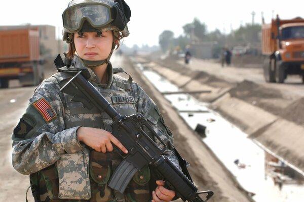 Ragazza soldato s uniforme militare con armi in mano sullo sfondo di veicoli di trasporto