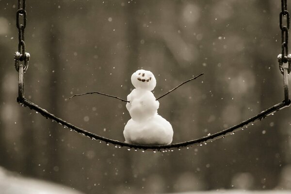 SCHNEEMANN SCHWINGT IM WINTER AUF EINER SCHAUKEL