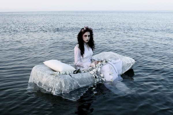 Photo shoot on the river in bed. A girl in a white dress