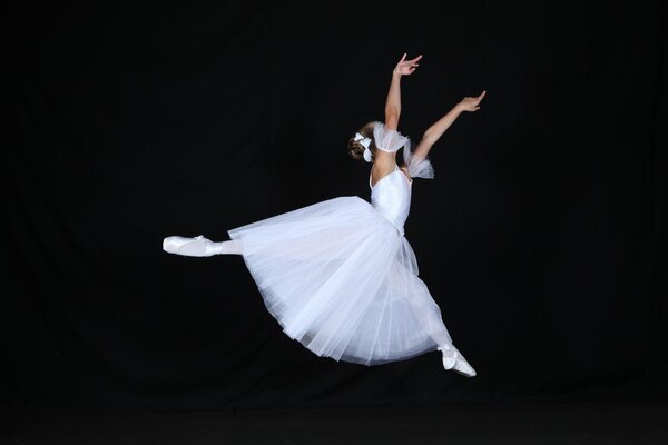 Bailarina de salto con un vestido blanco sobre un fondo negro