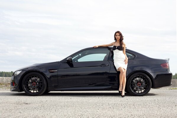 A girl in a beautiful dress next to a black BMW