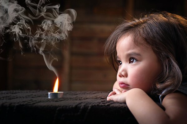 A little girl looks at the smoke from a candle