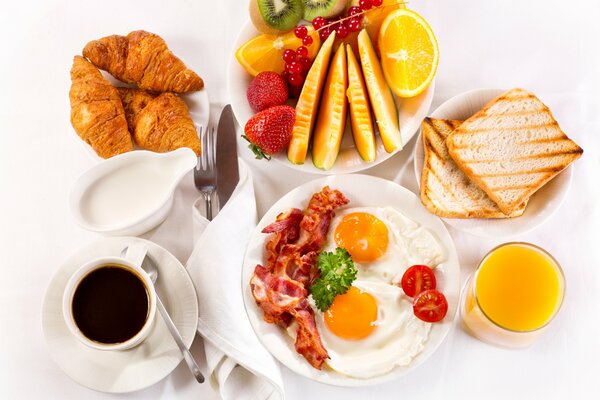 Das Frühstück wird auf dem Tisch mit Croissants serviert, Rührei mit Speck und Obst