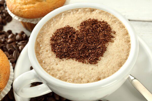 A cup of coffee with a chocolate heart and cupcakes