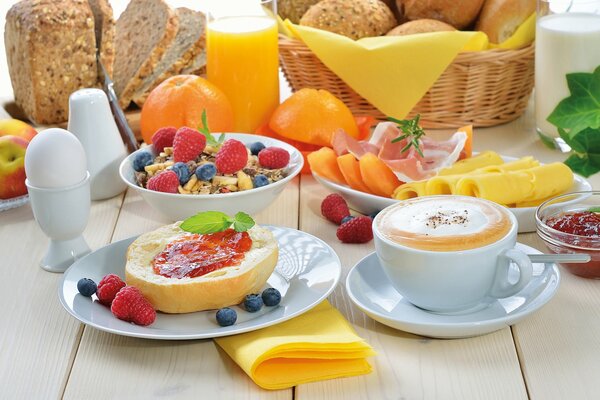 Frühstück bestehend aus weich gekochtem Ei, Toast mit Marmelade, Obst, Käse und einer Tasse Cappuccino