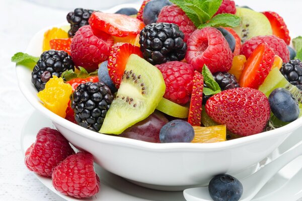 En un plato de postre en forma de ensalada de frutas de moras, fresas, frambuesas, kiwi