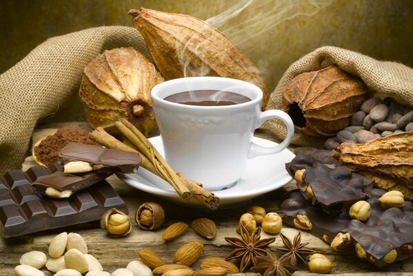 A mug of coffee with smoke. Surrounded by nuts and chocolate