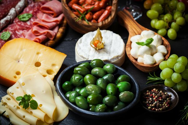 Table appétissante avec des collations sous la forme de divers fromages, fruits, jambon et olives