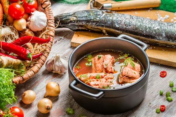 Orecchio in una casseruola su uno sfondo di pesce su un tagliere e un cesto con verdure