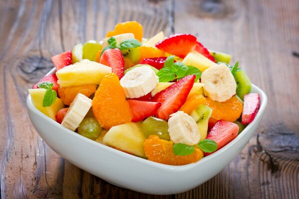 Dessert in the form of fruit salad with banana, tangerine, strawberry, pineapple and mint leaves