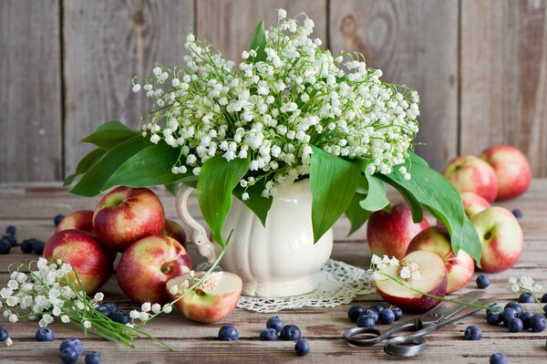 Zarte Maiglöckchen auf einem Hintergrund von Äpfeln und Blaubeeren