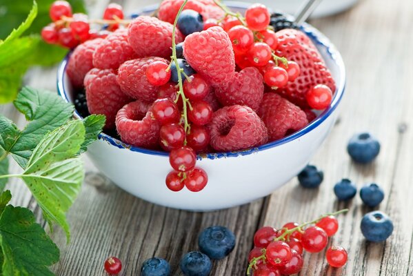 Auf dem Tisch steht eine Schüssel, in der Erdbeeren, Blaubeeren, Himbeeren liegen