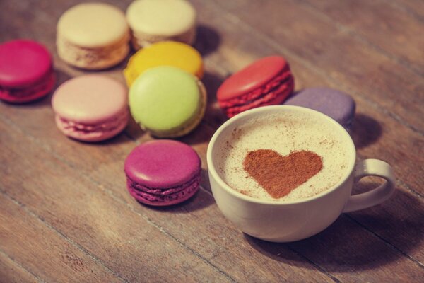 Macarrones en la mesa junto al café cremoso en una taza con espuma en la que el corazón