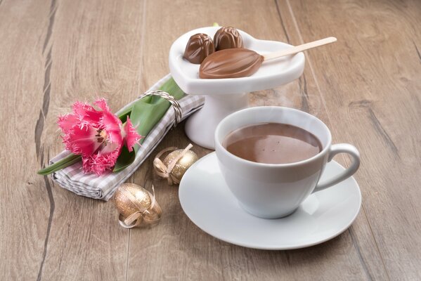 A mug of fragrant coffee with sweets and a flower