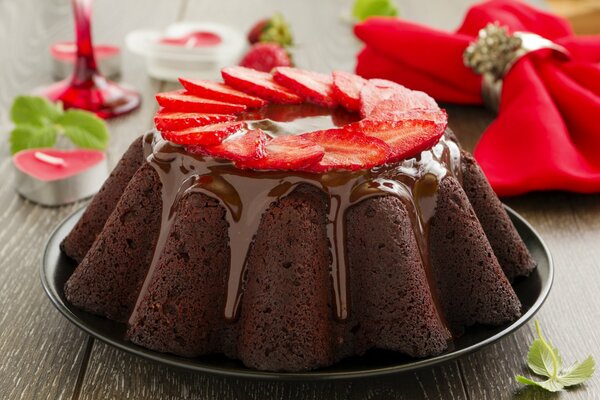 Mit Glasur und Erdbeeren geschmückter Cupcake vor dem Hintergrund von Servietten und Kerzen