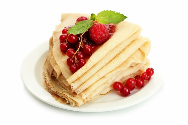 Crêpes sur une assiette avec des groseilles, des framboises et de la menthe