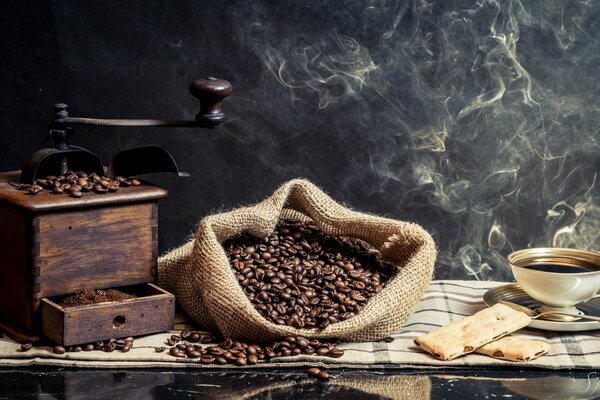 A bag of coffee beans on the table next to a cup and a coffee grinder