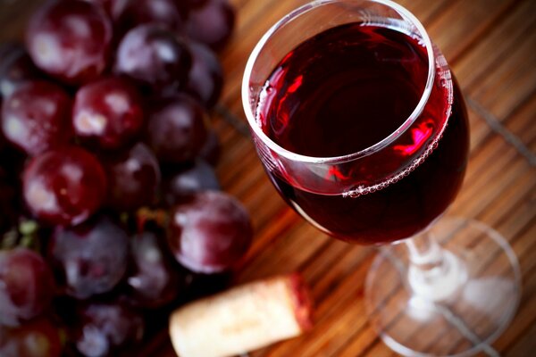 A glass of grape wine and grapes lying on the table