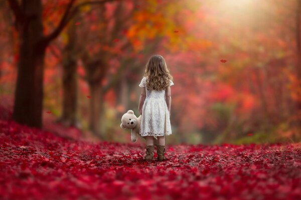 Una niña con un oso de peluche en el fondo de un paisaje de otoño