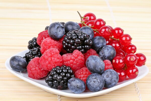 A plate of various berries raspberries blueberries currants