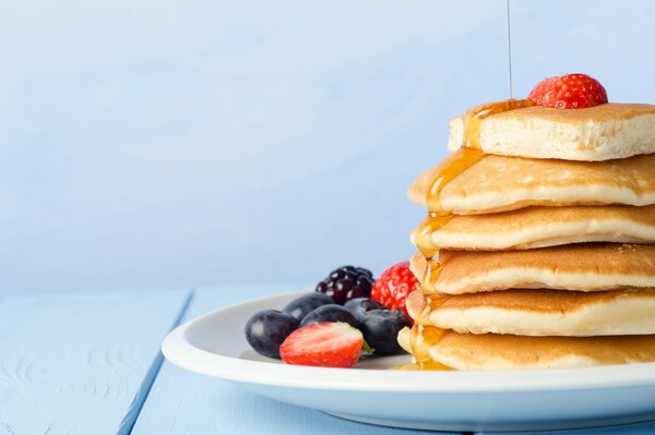 Pancakes on a plate, drizzled with honey, with blueberries, blackberries and strawberries