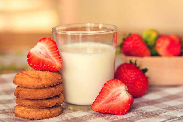 Junto a un vaso de leche se encuentran galletas y fresas