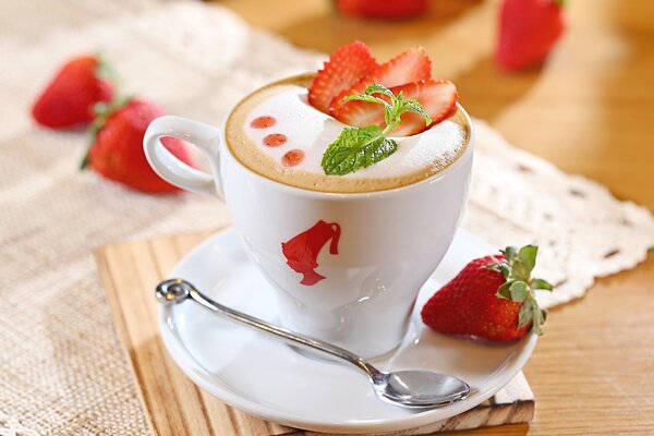 Una taza de capuchino fragante con fresas en la mesa