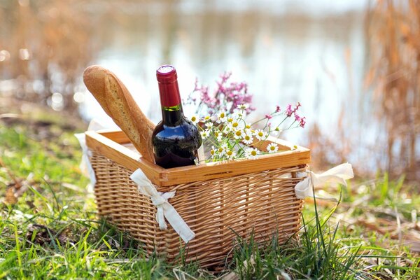 Cesto da picnic con vino e baguette sulla riva