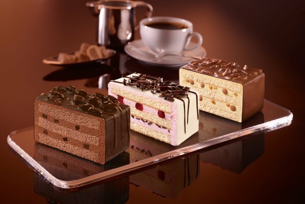 Three different cakes, with icing, strawberry and walnut on the background of a tea set with a kettle and sugar